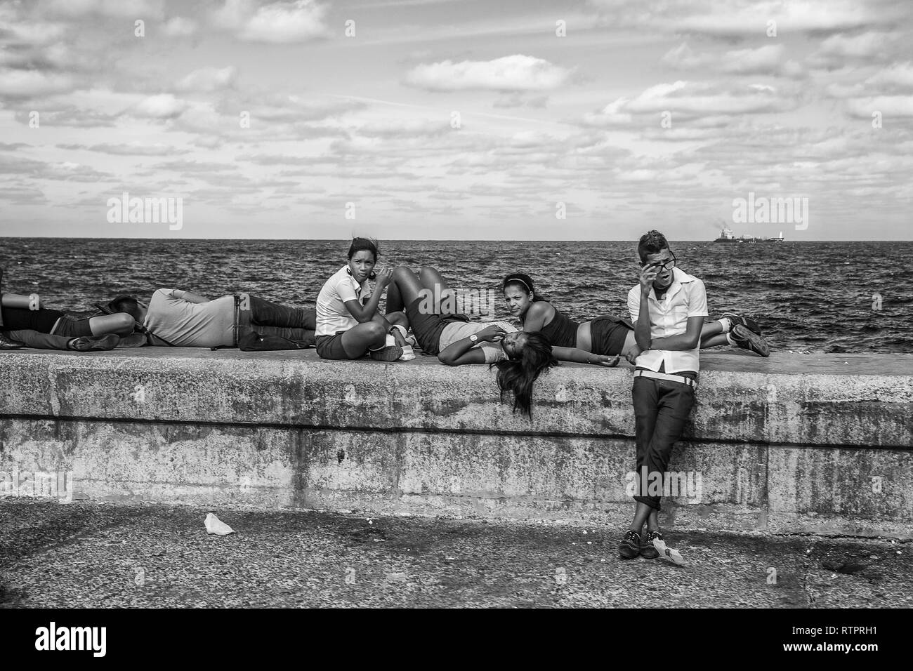 Havana, Cuba - 22 January 2013: A view of the streets of the city with cuban people. A group of teenagers relaxed on seawall malecon. Stock Photo