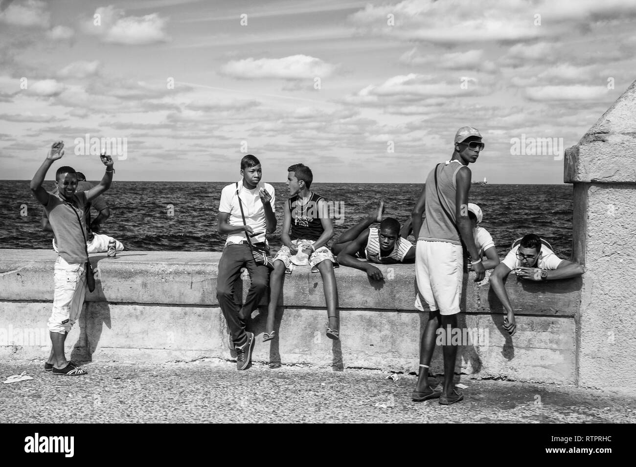Havana, Cuba - 22 January 2013: A view of the streets of the city with cuban people. A group of teenagers relaxed on seawall malecon. Stock Photo