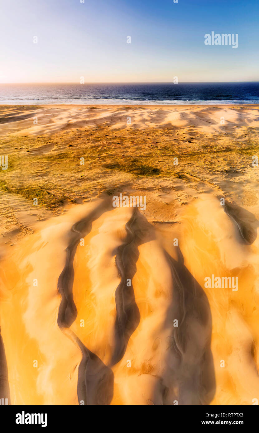 Backs of erodes sand dunes of Stockton beach in lead up to waterfront of Pacific ocean - aerial vertical panorama from ground surface to distant sky a Stock Photo