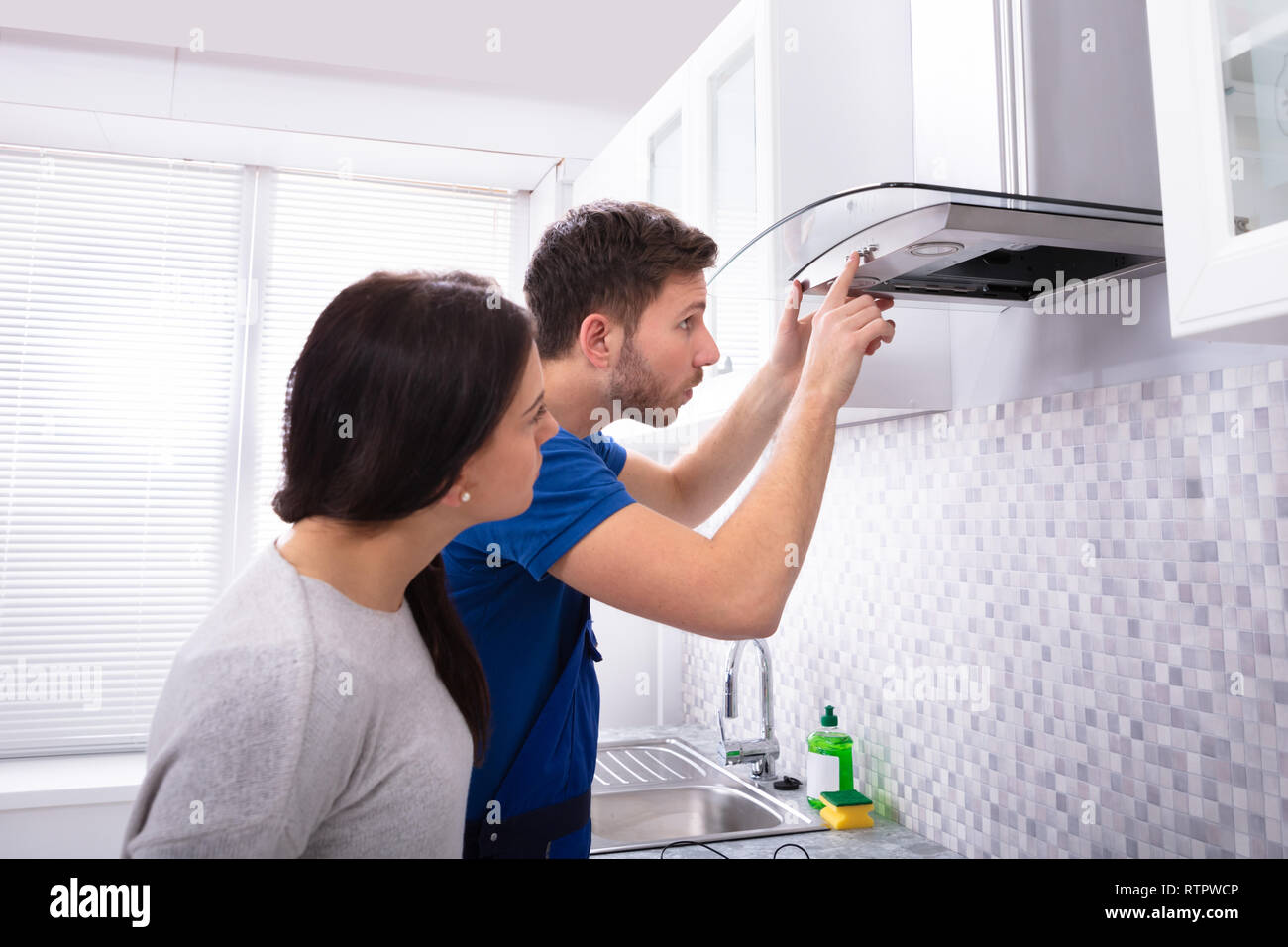 Pretty Young Woman Looking At Repairman Fixing Kitchen Extractor Filter ...