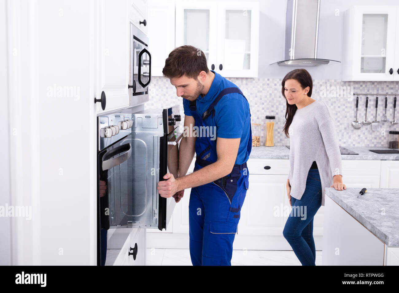 Beautiful Woman Looking At Young Serviceman Installing Oven In Kitchen Stock Photo