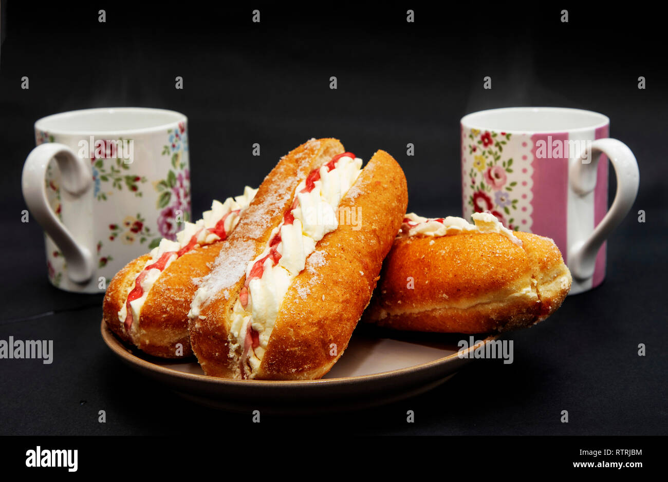 Cream and Jam Doughnuts on a Plate beside Two Mugs of Tea Stock Photo
