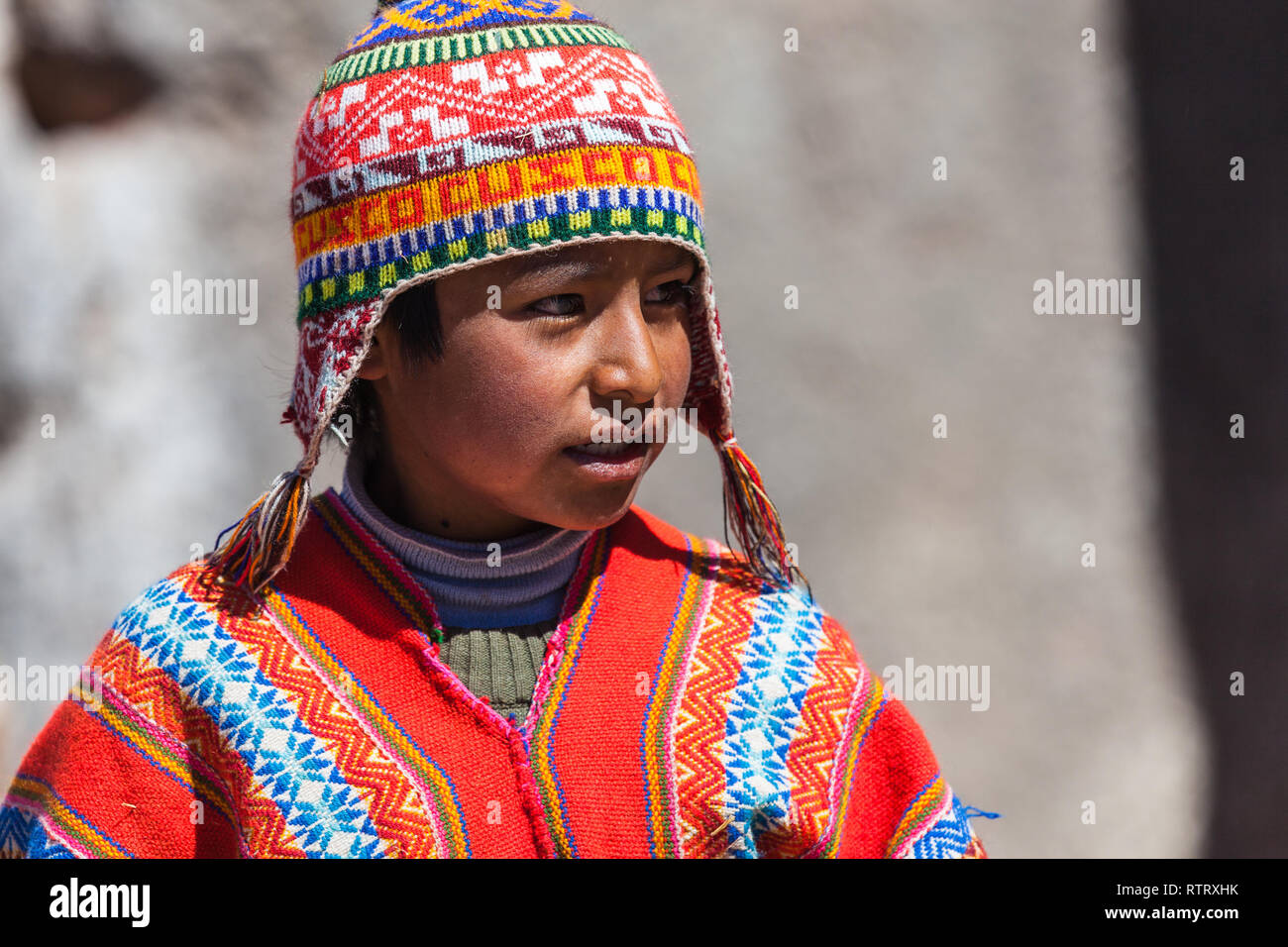 Cusco, Peru, July 2018: Child native to Cusco, with his typical cap and poncho, looks to the side while the photographer takes photos. Stock Photo