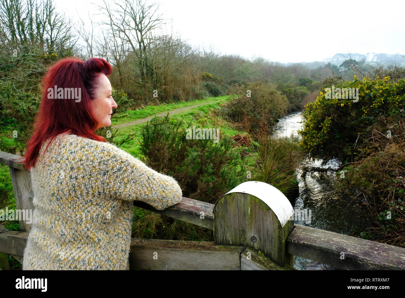 Mature woman leaning on a bridge and watching a river - John Gollop Stock Photo