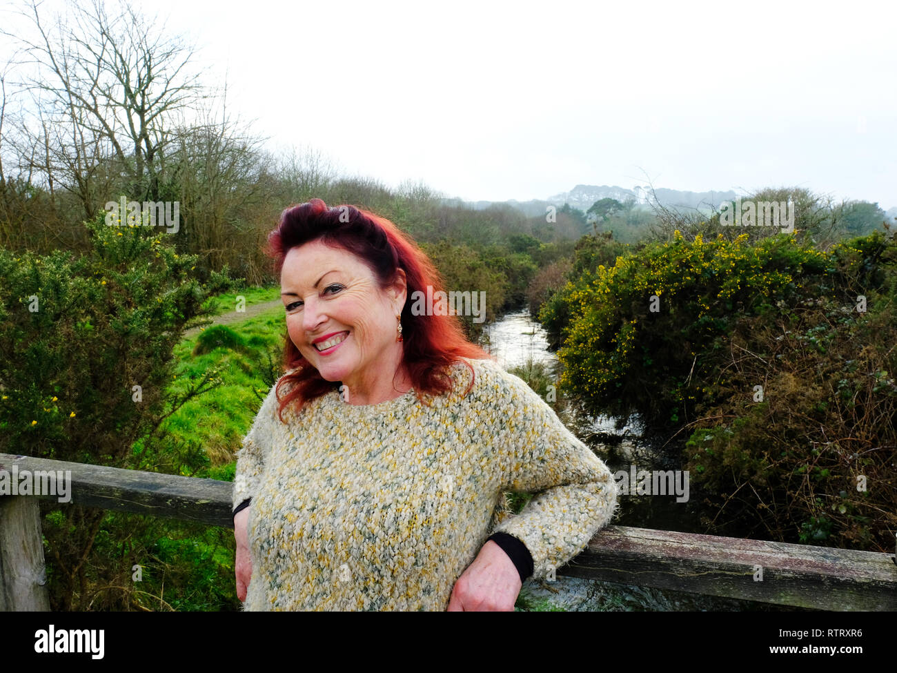 Mature woman smiling at camera, standing on a bridge - John Gollop Stock Photo