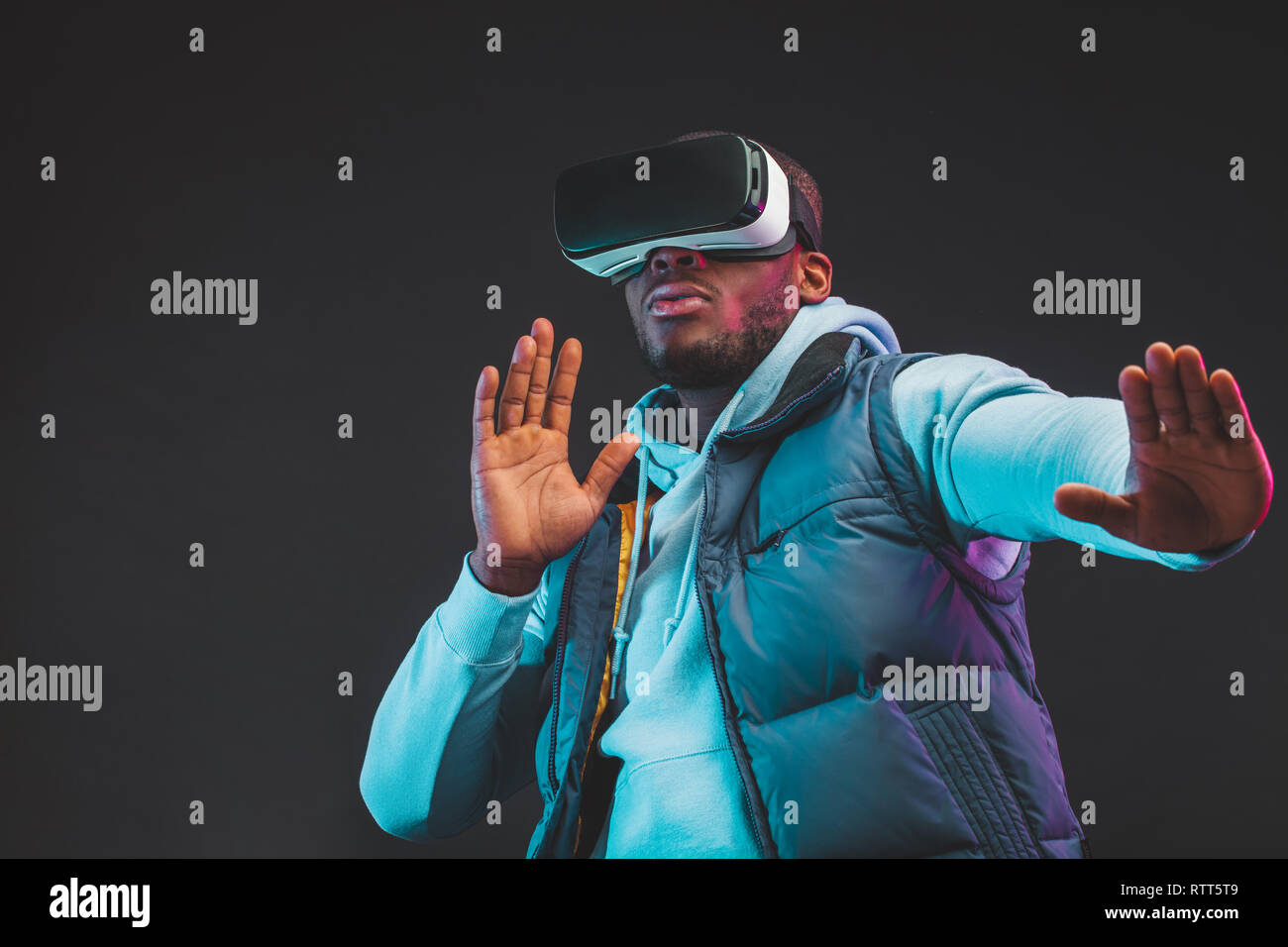 Gaming concept. African casual man in warm seasonal outdoor clothes wearing mobile VR headset enjoying new reality in dark room. Fashion and Innovatio Stock Photo