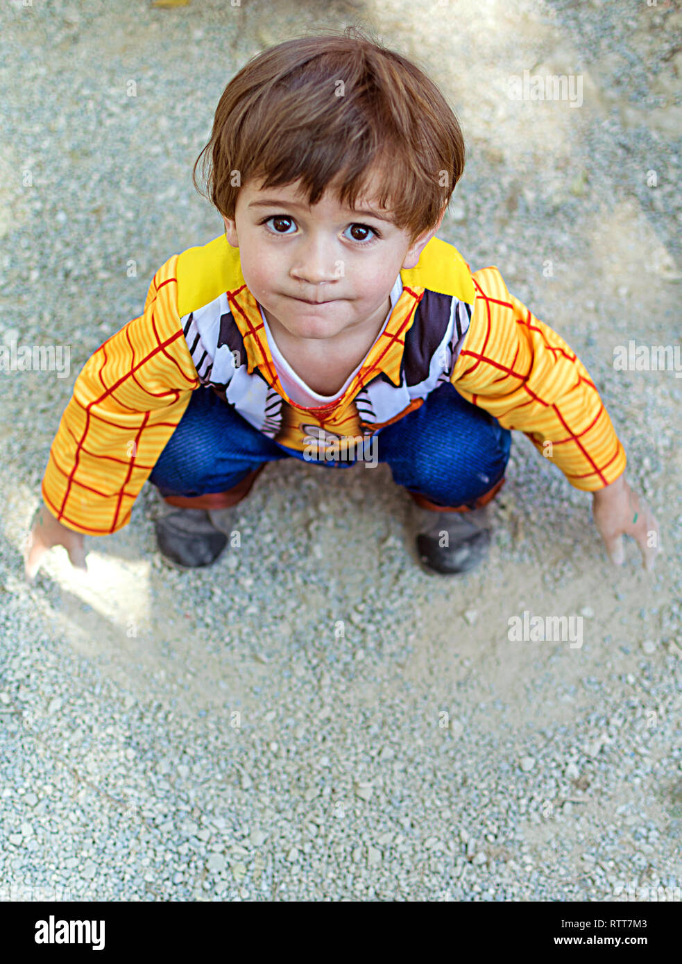 Little kid, child, children wearing woody toy story costume playing on the ground with the dirt and sand, dirty hands. Childhood creativity in Spain in 2019. Stock Photo
