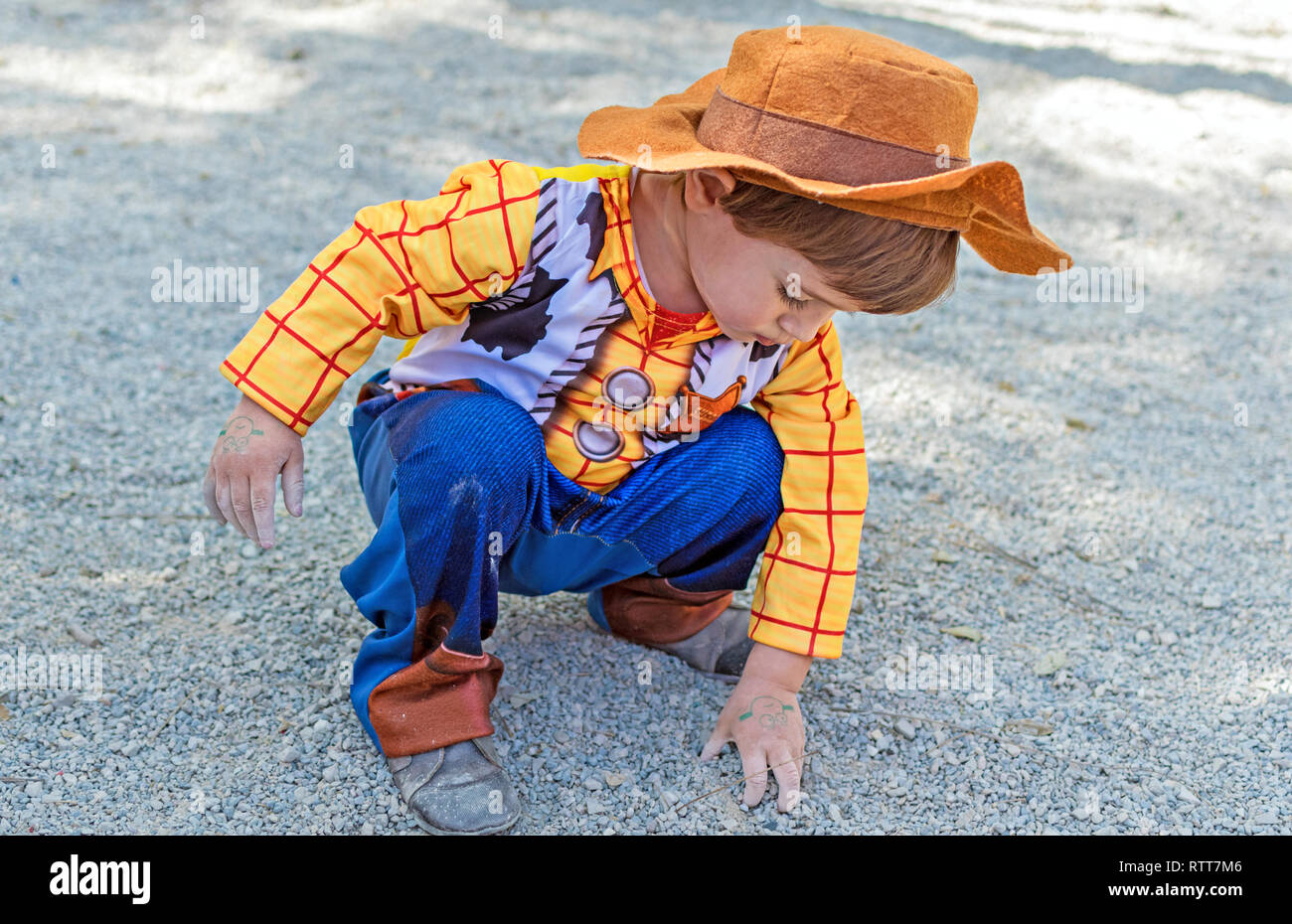 Little kid, child, children wearing woody toy story costume playing on the ground with the dirt and sand, dirty hands. Childhood creativity in Spain in 2019. Stock Photo