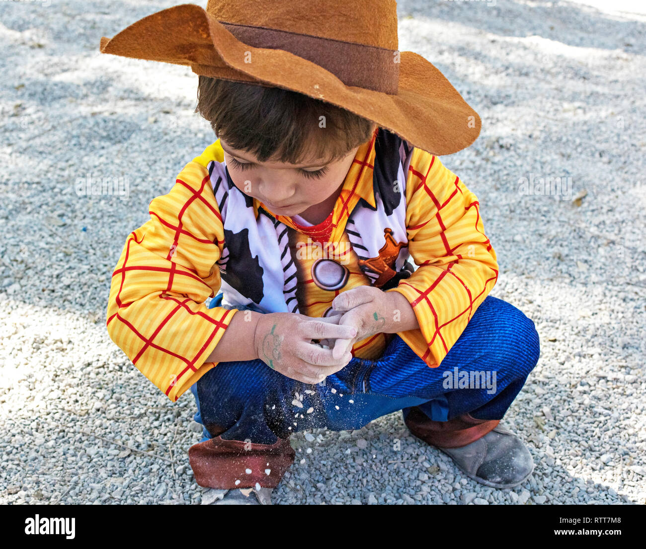 Little kid, child, children wearing woody toy story costume playing on the ground with the dirt and sand, dirty hands. Childhood creativity in Spain in 2019. Stock Photo