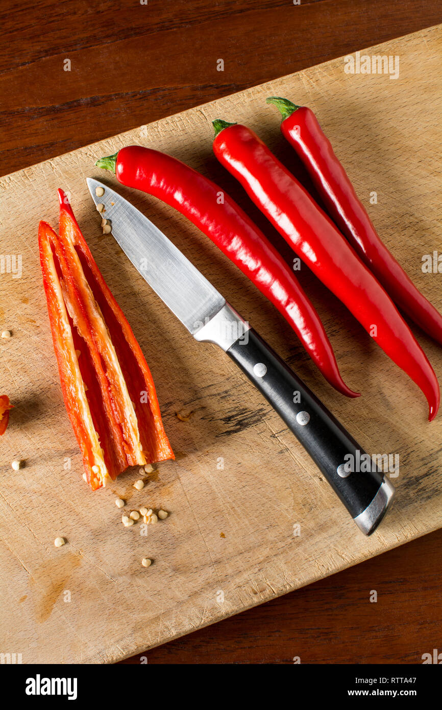 Deseeding Red hot chilli peppers on a carving board with knife Stock Photo