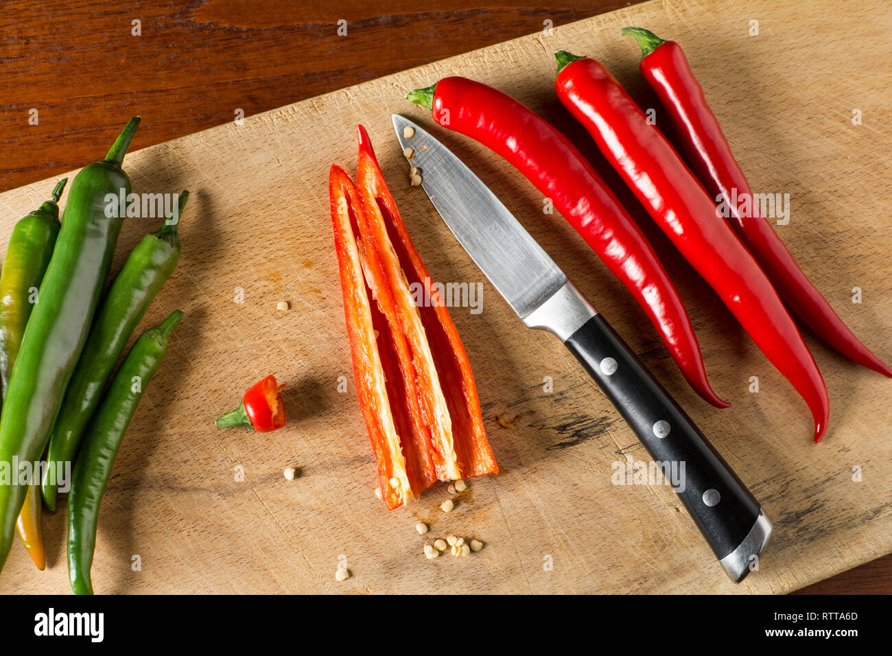 Deseeding Red and green hot chilli peppers on a carving board with knife Stock Photo