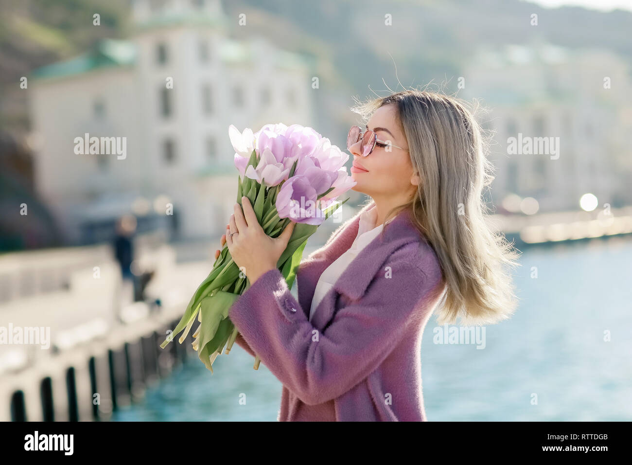 Beautiful happy woman with straight hair holding a bouquet of pink tulips one spring sunny day. Stock Photo