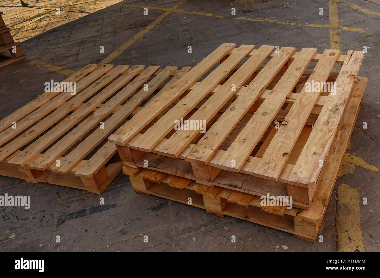 Three wooden pallets stacked on the floor which has yellow markings