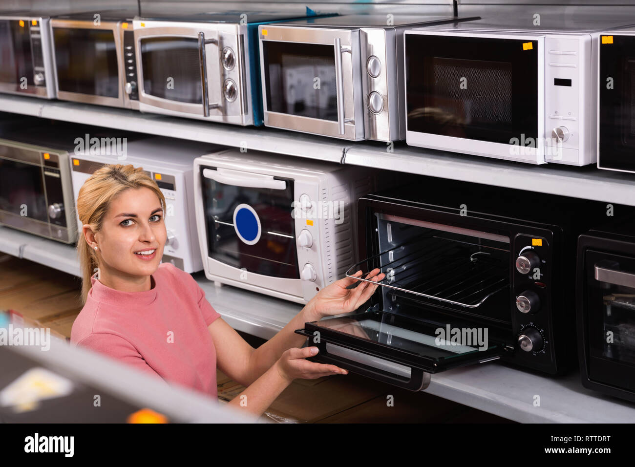 Positive glad cheerful female looking new microwave for kitchen in furniture store Stock Photo