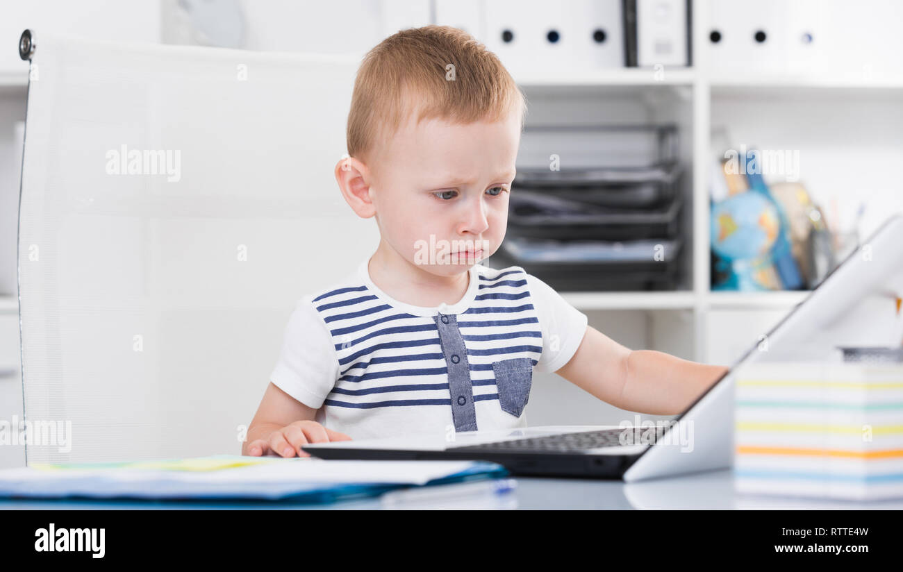 Young cute boy is watching cartoons on laptop in the office. Stock Photo