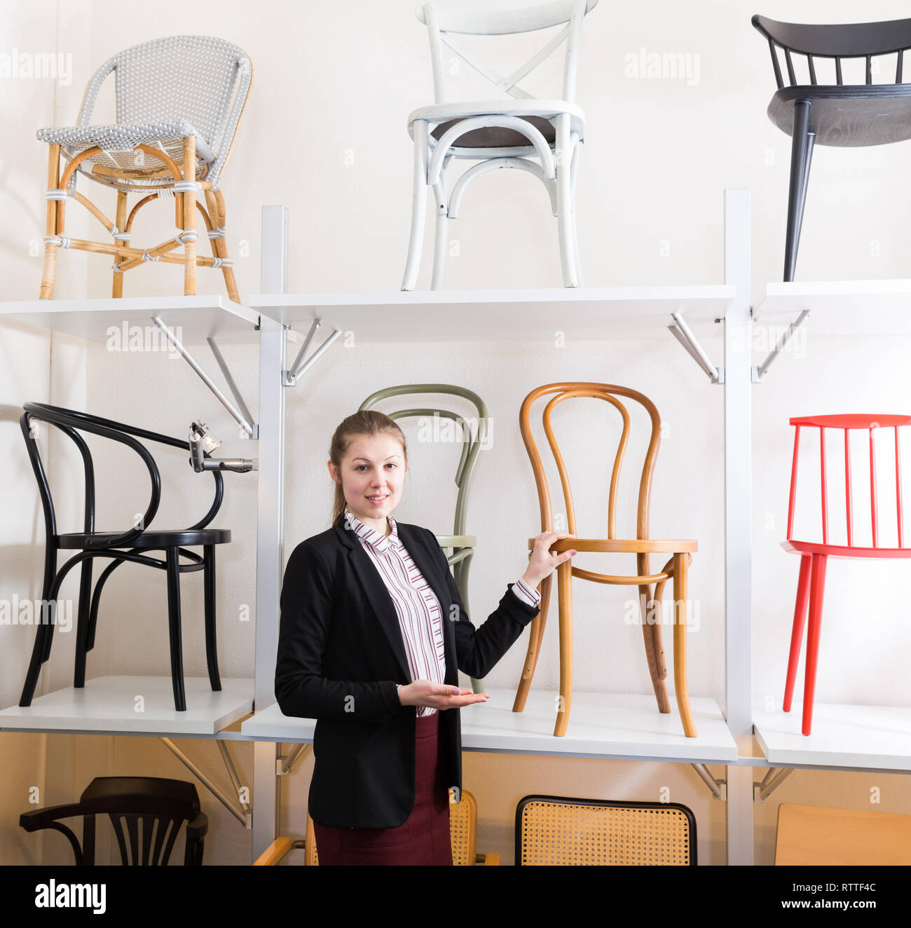 Young polite saleswoman offering original wooden chairs in furniture store Stock Photo Alamy