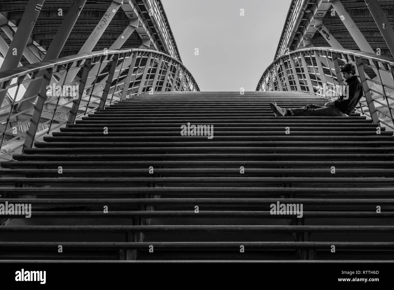 A young man sits silently, deep in thought on a bridge stairway in Paris. Stock Photo