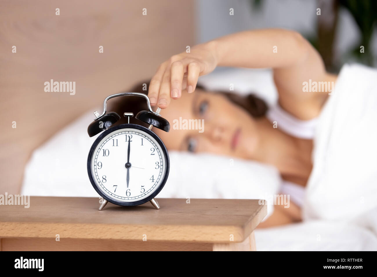 Young woman lying in bed, woken by alarm signal, turning off clock Stock Photo
