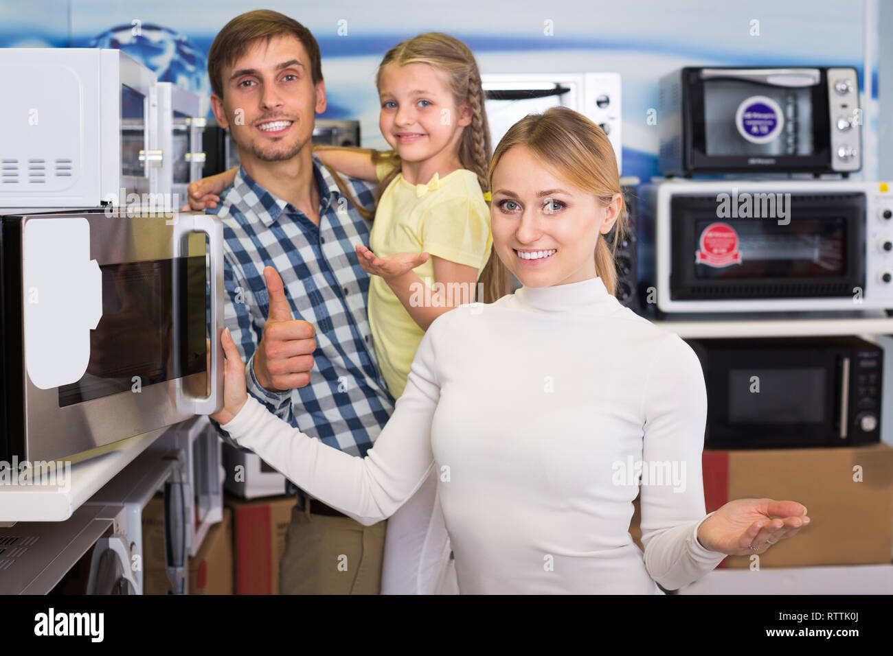 Smiling couple with kid choosing microwave oven in hypermarket Stock Photo