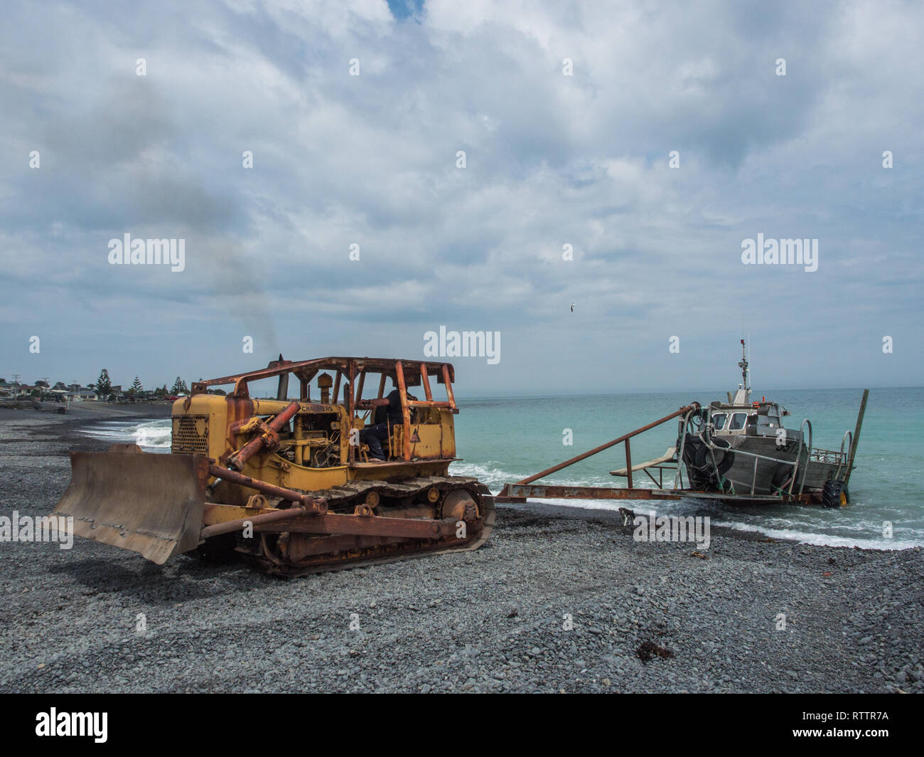 Bulldozer hauling fishing boat ashore, shingle beach, exposed coast, Ngawi, Palliser Bay, Wairarapa, New Zealand Stock Photo