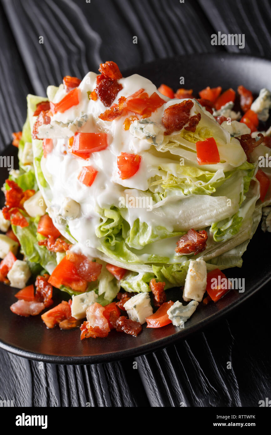 American Wedge Salad with iceberg lettuce, blue cheese dressing, crunchy bacon, and fresh tomatoes closeup on a plate on the table. Vertical Stock Photo