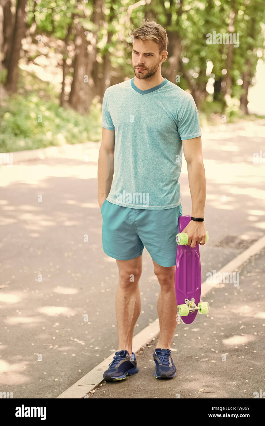 Still childish. Guy carries penny board, ready to ride. Man calm face  carries penny board park nature background, defocused. Man likes to ride  skateboard and sporty lifestyle. Hobby concept Stock Photo -