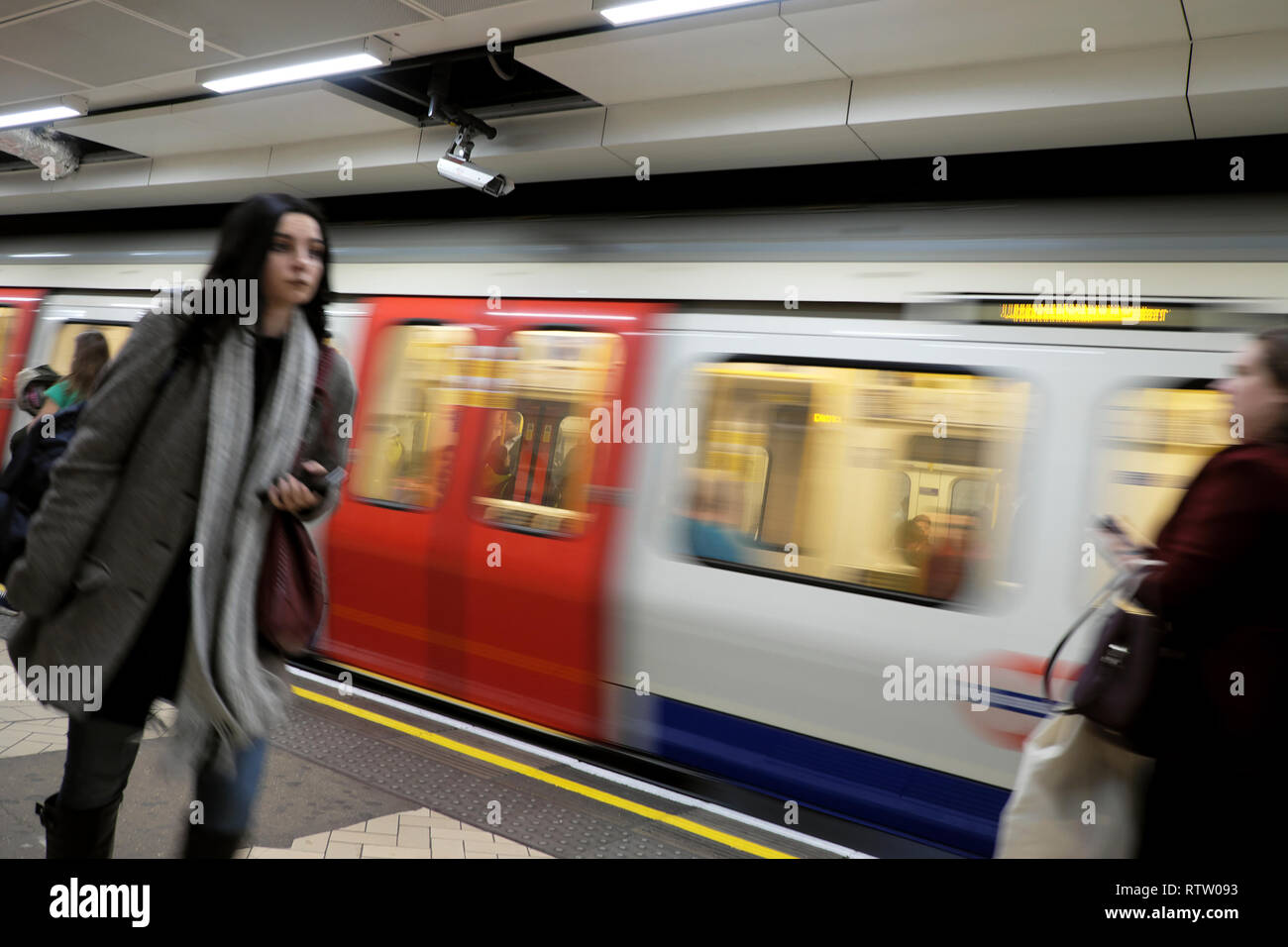 London underground tube train in motion and female passenger walking along platform at Brixton station in South London UK  KATHY DEWITT Stock Photo