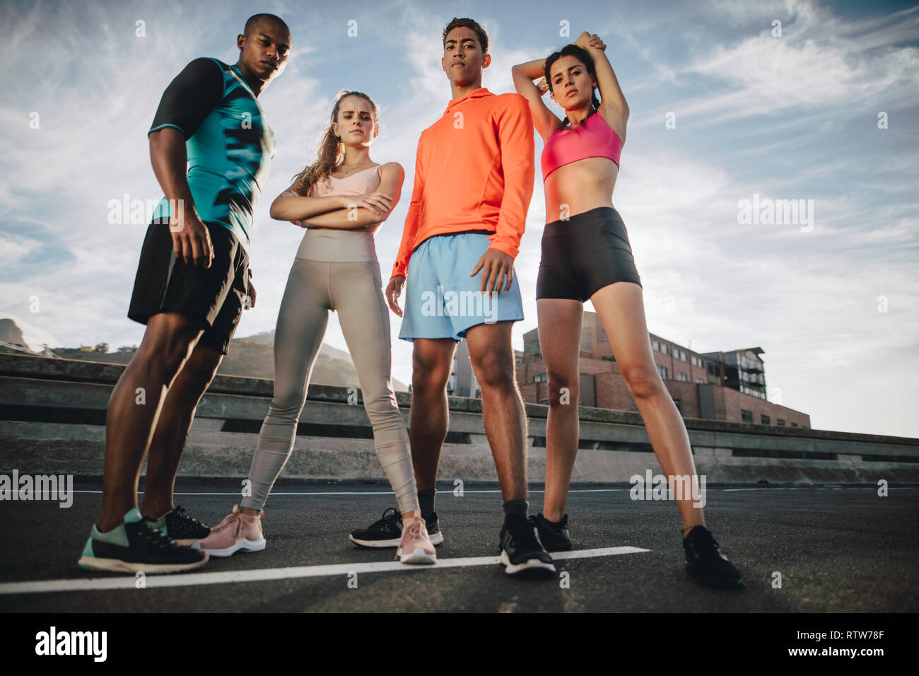 Full length of mixed race friends standing outdoors on the city street after workout. Fitness group standing together after workout. Low angle shot. Stock Photo