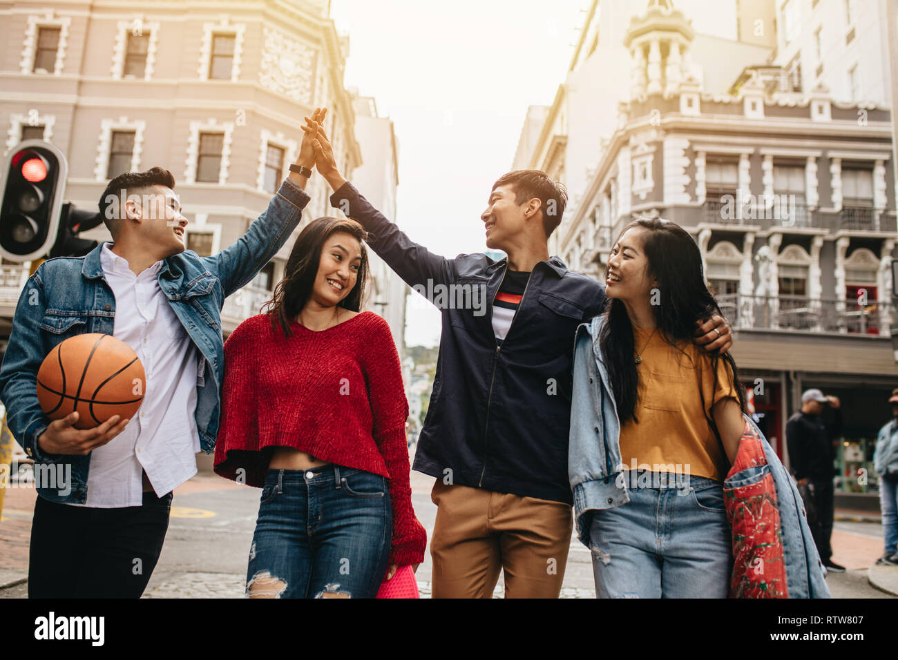 Aisan young friends having fun together on the street, men high fiving each other. Group of men and women walking outdoors. Stock Photo