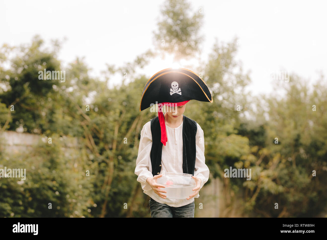 Boy dressed up as pirates walking with fish bowl outdoors. Boy playing as pirates outdoors. Stock Photo