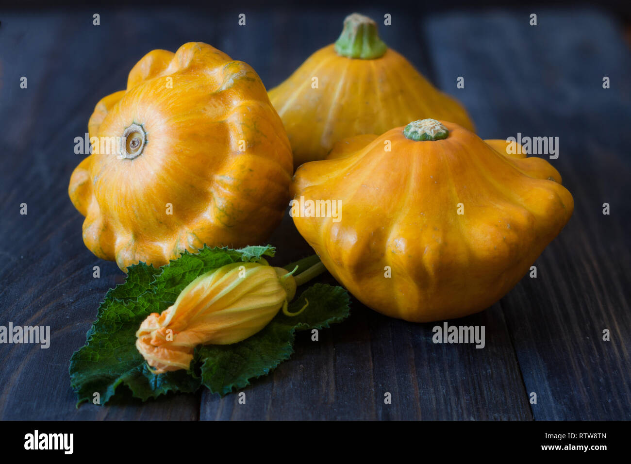 three yellow pattypan squash with leaf and flower on a dark wooden