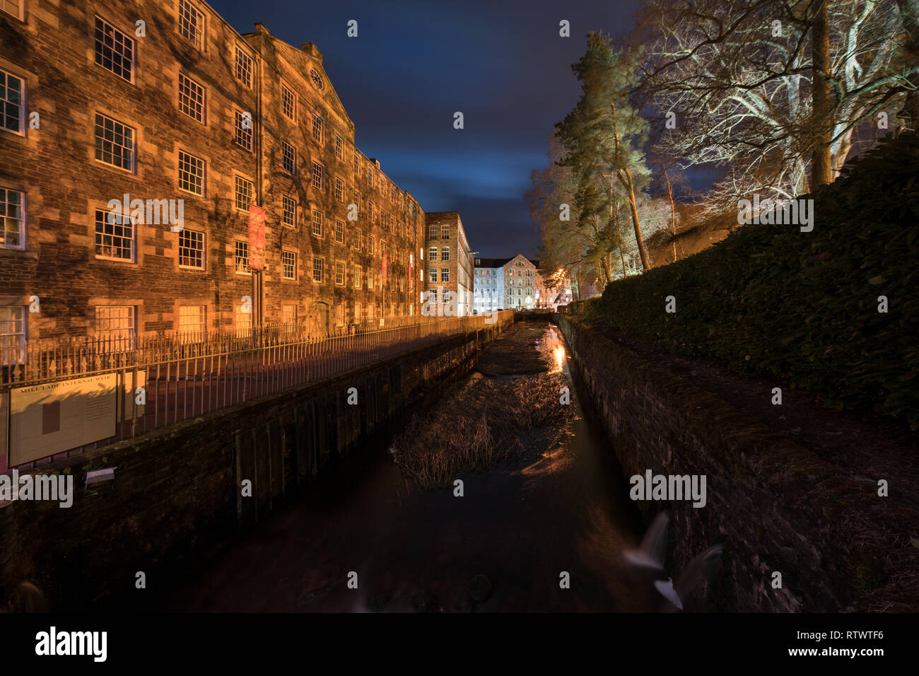 New Lanark World Heritage Site seen at night showing buildings illuminated and lights showing in windows. Stock Photo