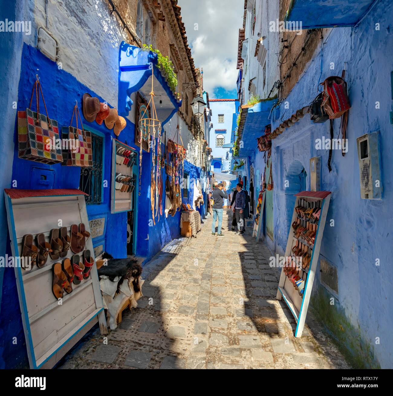 Sale of leather sandals in narrow lane with blue houses, Medina of