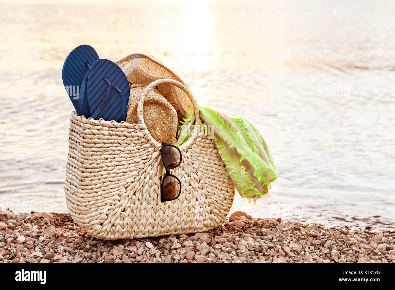 Straw Bag, Hat, Sunglasses And Flip Flops On The Shore At Sunset In The Summer Stock Photo