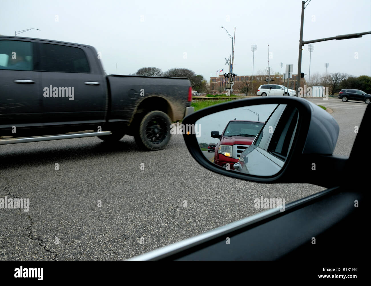 Side view mirror on an overcast day in Texas; reflection of red car in rear at a stop light and a truck driving by headed in the opposite direction. Stock Photo