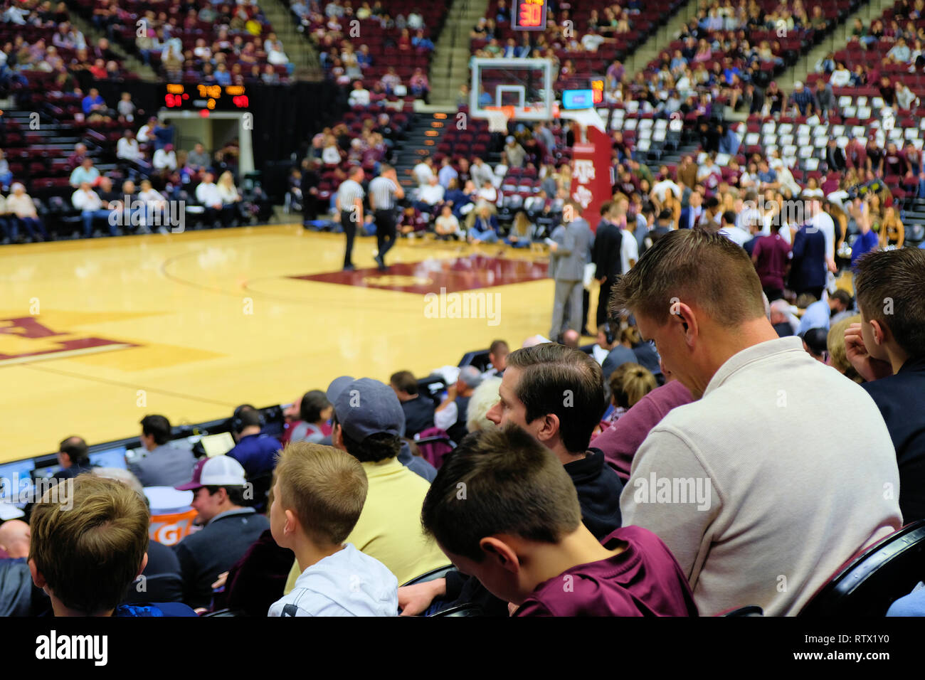 Family of fans watching arena floor during an NCAA basketball game at