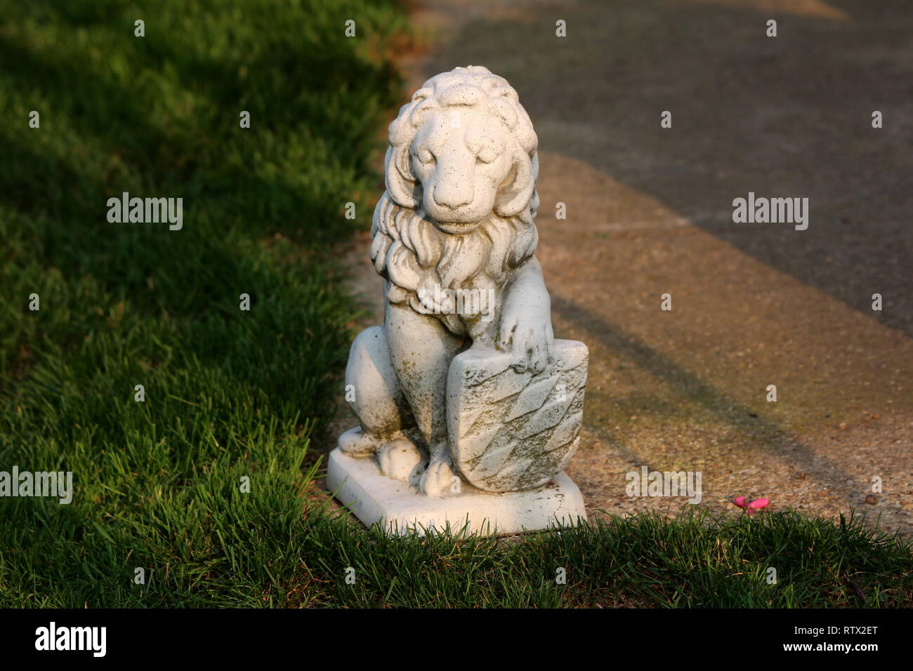 Concrete sculpture of mighty lion holding shield on edge of concrete path surrounded with grass