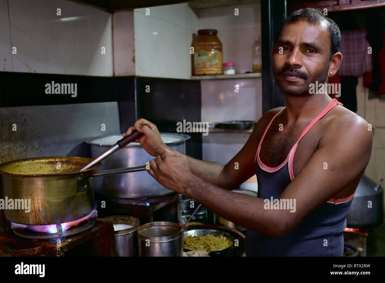 An employee in a small tea house in Mumbai, India, in Indian fashion boiling water, milk, tea