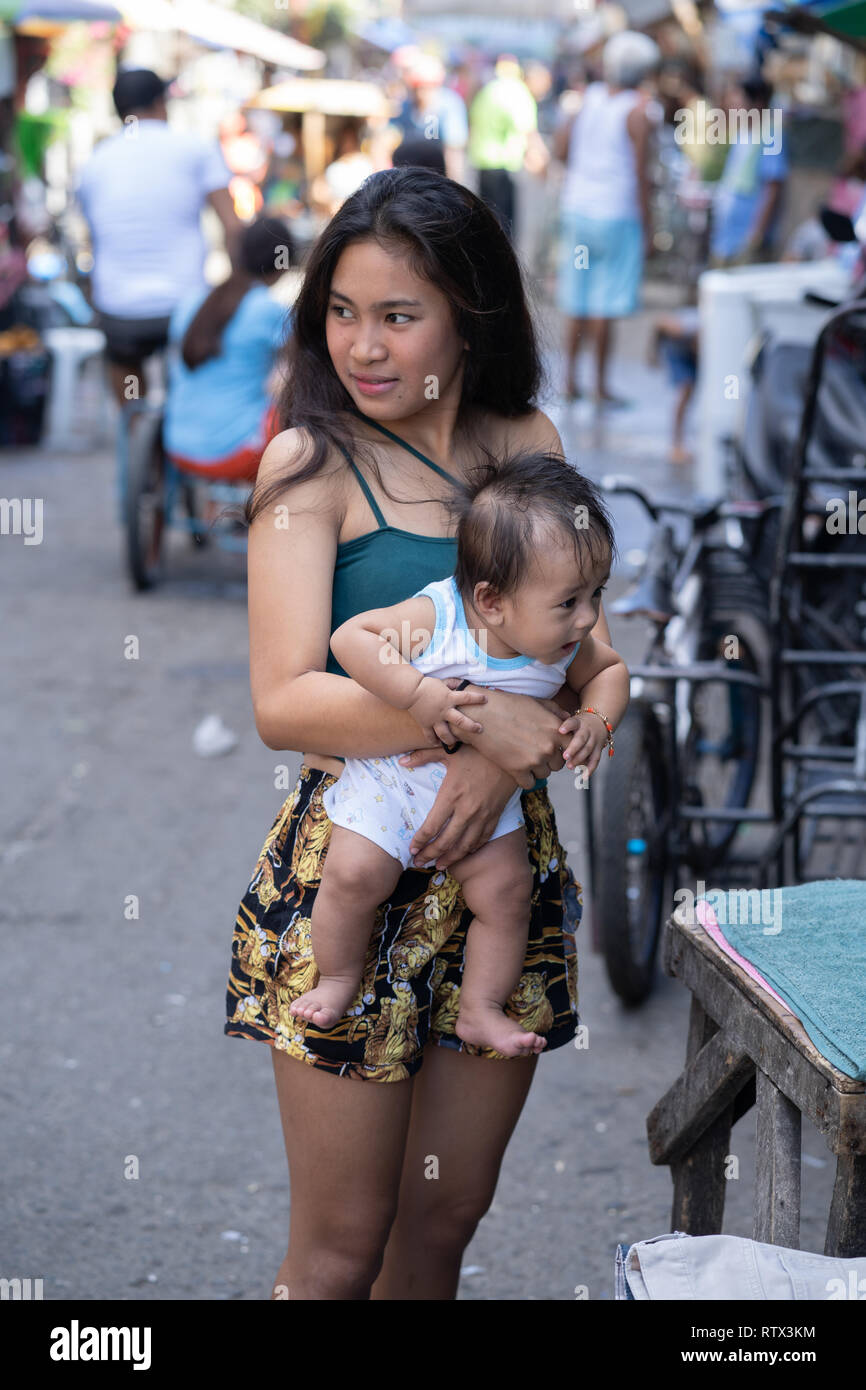 A young Filipina girl carries a baby within a slum area of Cebu City,Philippines Stock Photo