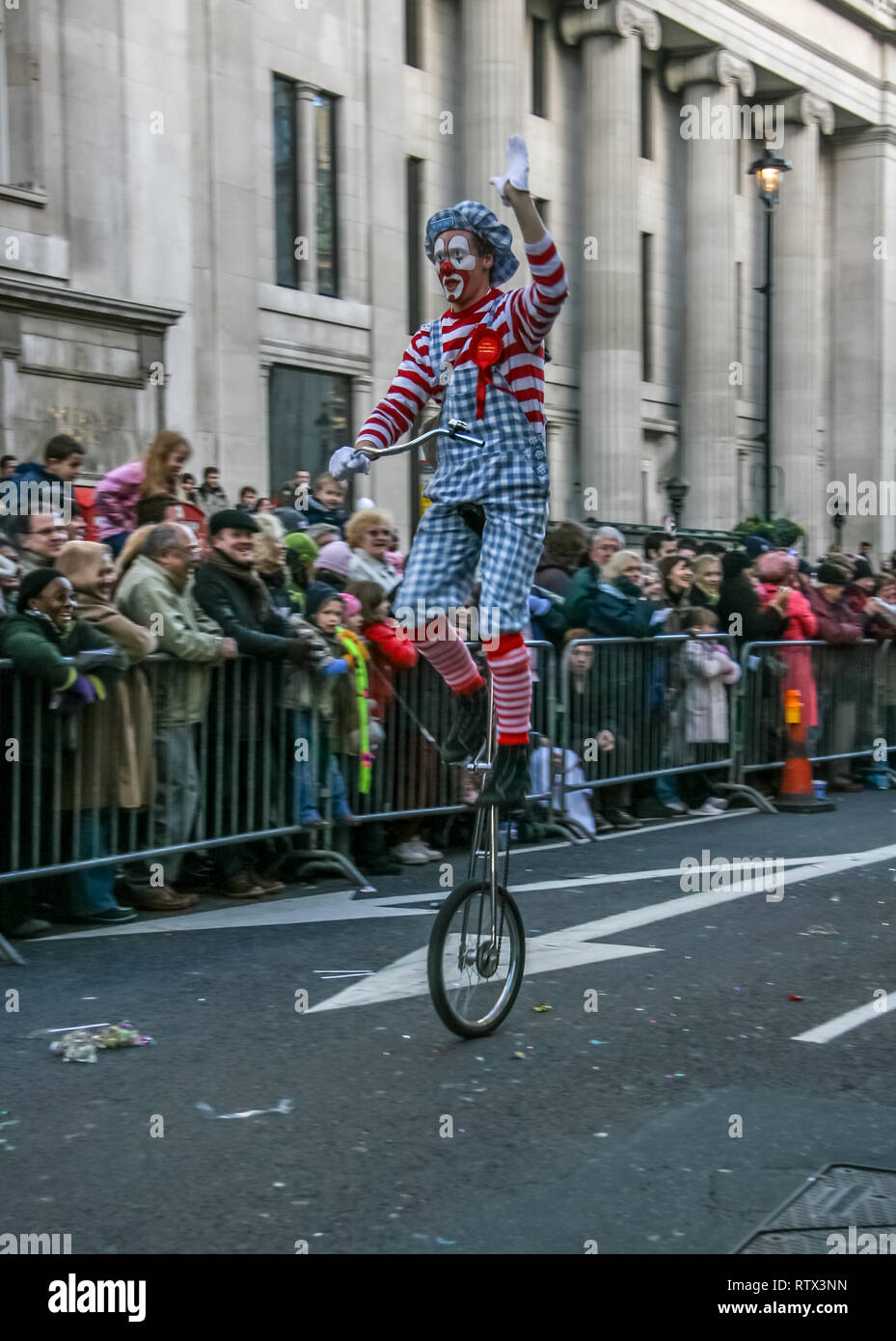 London, United Kingdom - January 1, 2007: Man in clown costume rides unicycle, and waves to cheering crowd, during New Year's Day Parade. Stock Photo
