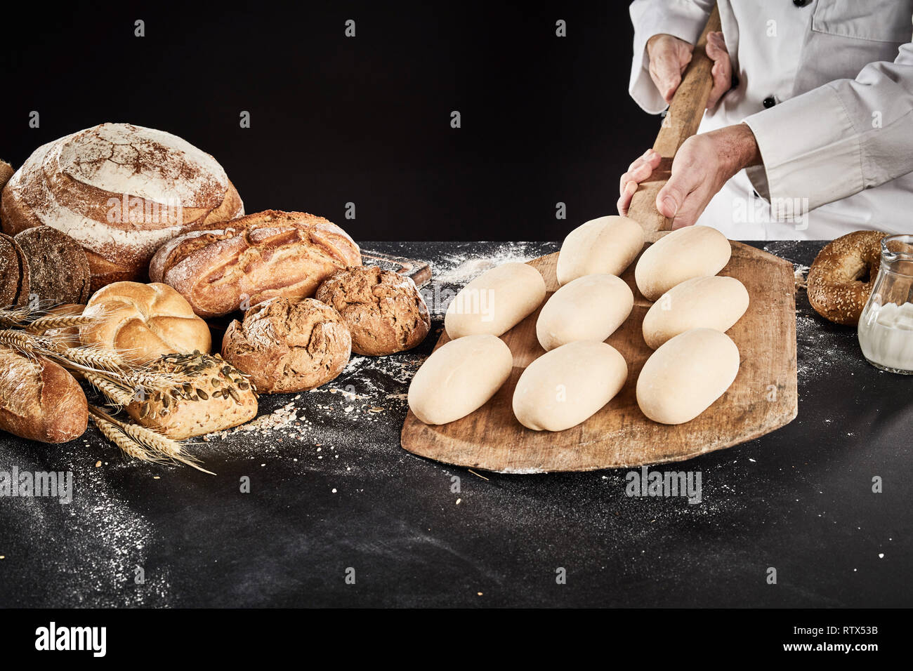 Ready to cook loaves of bread dough on a wooden paddle held by a chef