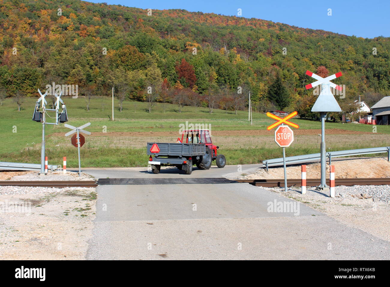 Tractor pulling trailer over railroad tracks crossing paved road surrounded  with stop and warning road signs with grass and colorful forest Stock Photo  - Alamy