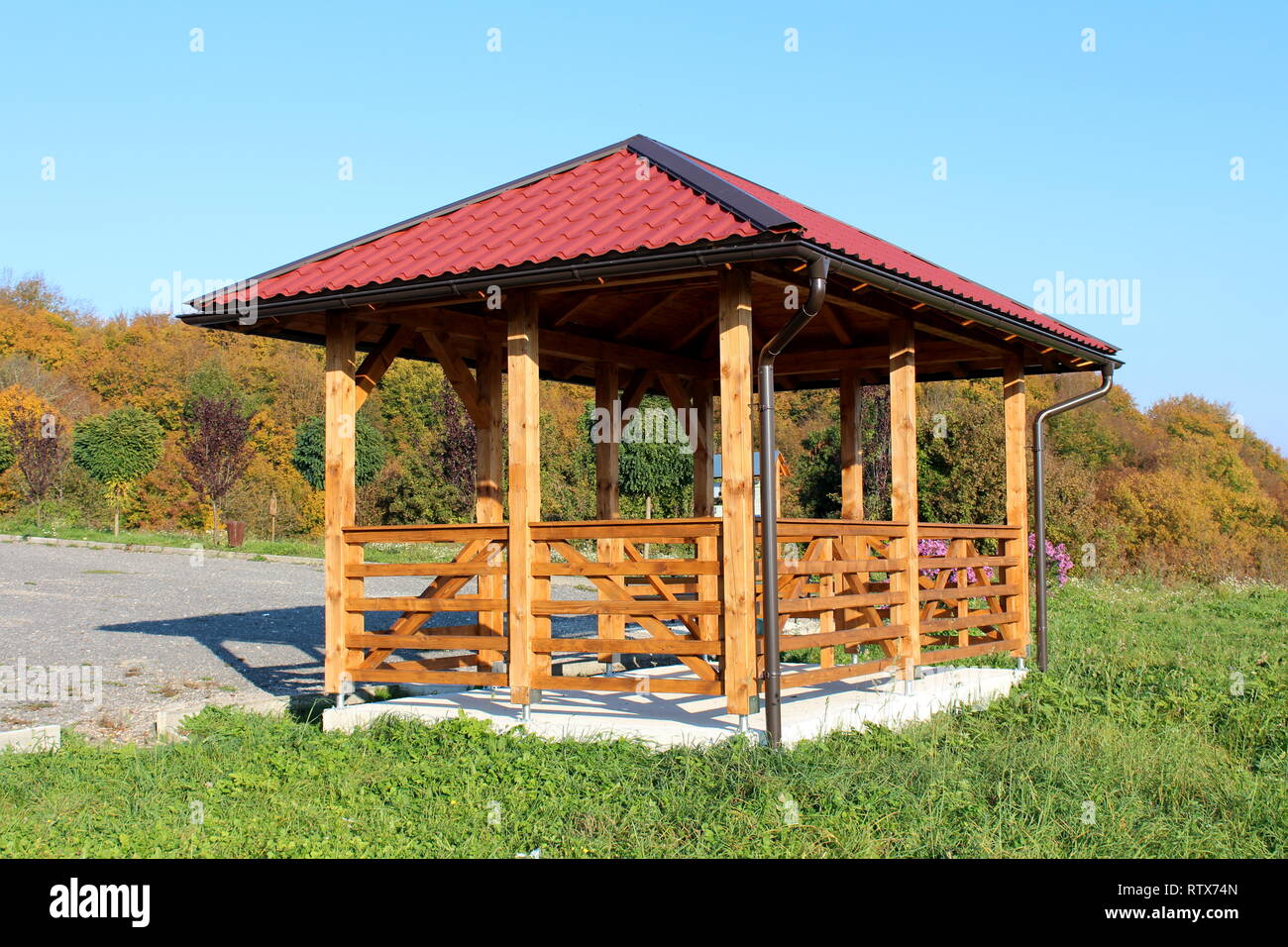 Wooden gazebo structure with new roof and gutter mounted on concrete foundation next to uncut