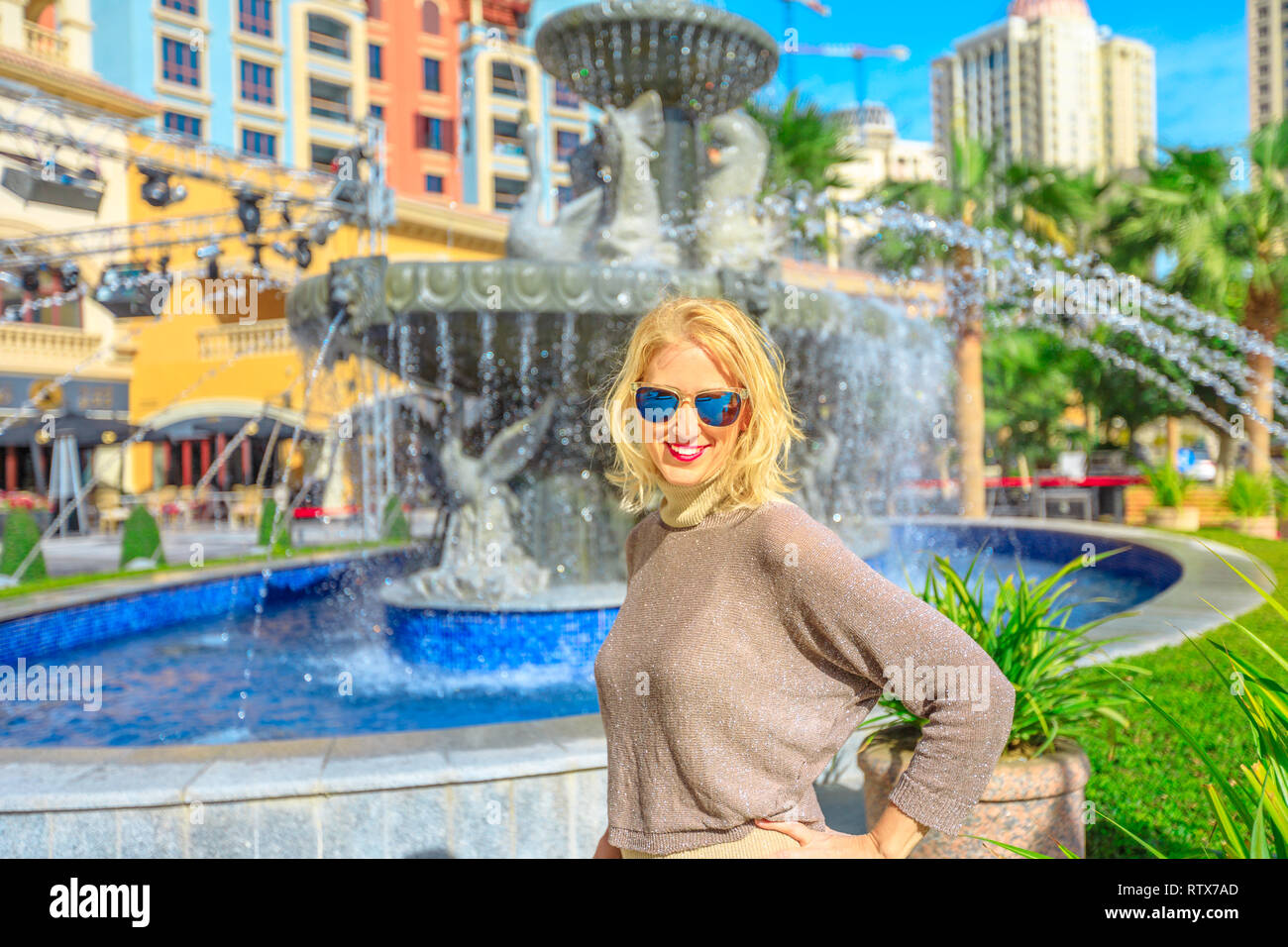 Happy blonde woman enjoys water fountain in Central Medina, an exclusive residential area in The Pearl Qatar, icon of Doha, Persian Gulf, Middle East Stock Photo