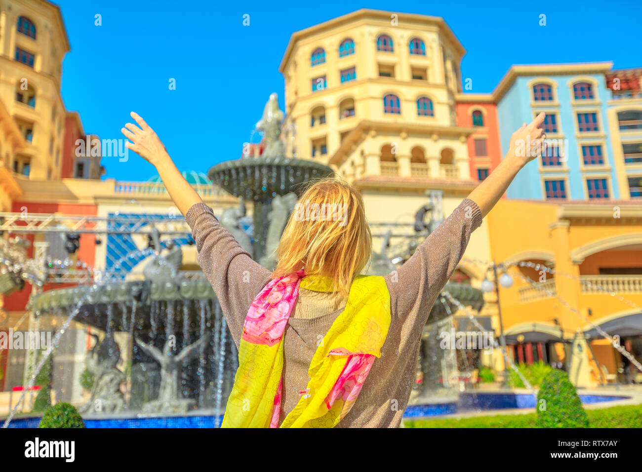 Carefree blonde woman enjoys water fountains in Central Medina, an exclusive residential area in The Pearl Qatar, icon of Doha, Persian Gulf, Middle Stock Photo