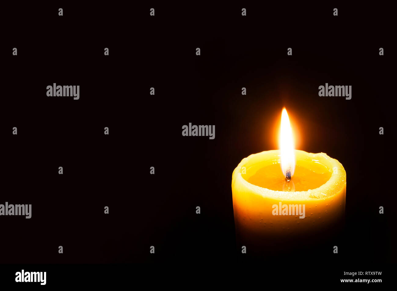 Single Burning Yellow Candle Glowing on a Dark Background. Copy Space