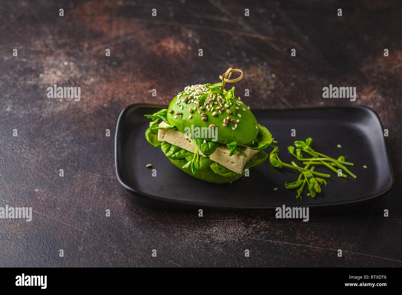 Vegan avocado tofu burger on black dish, dark background. Healthy detox food, plant based food concept. Stock Photo