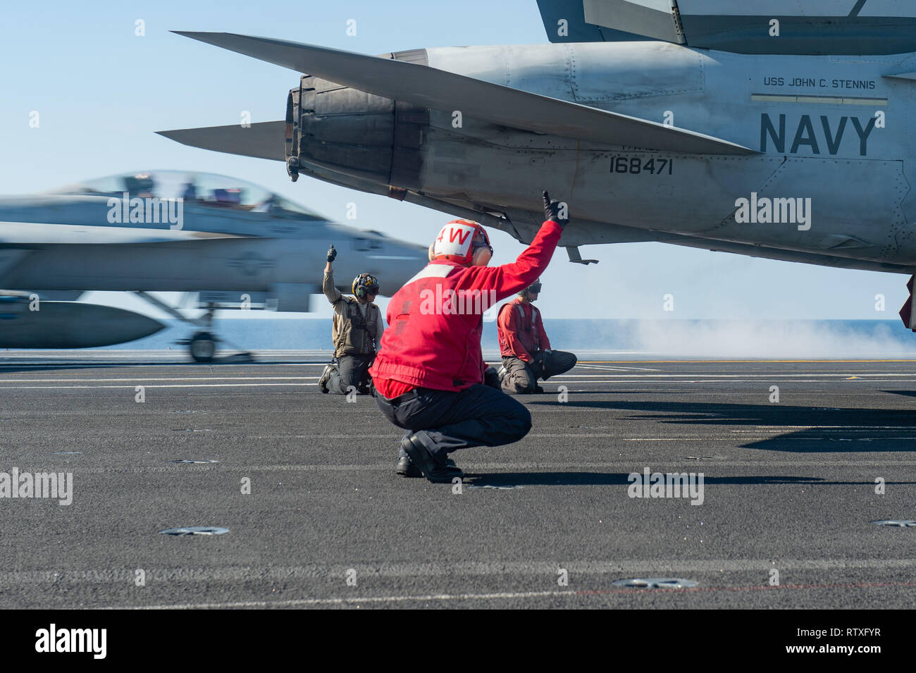 U.S. Sailors signal to launch an F/A-18E Super Hornet, assigned to Strike Fighter Squadron (VFA) 151, as an F/A-18F Super Hornet, assigned to Strike Fighter Squadron (VFA) 41, launches from the flight deck of the aircraft carrier USS John C. Stennis (CVN 74) in the South China Sea, March 2, 2019. The John C. Stennis is deployed in the U.S. 7th Fleet area of operations in support of security and stability in the Indo-Pacific region. (U.S. Navy photo by Mass Communication Specialist Seaman Jeffery L. Southerland) Stock Photo