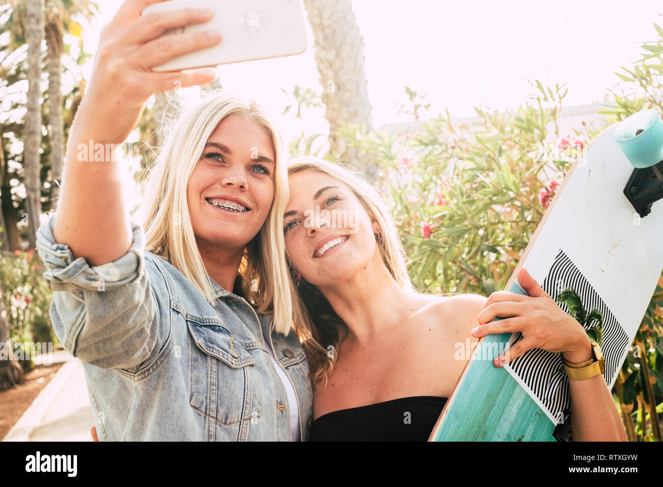 Happy coule of young caucasian attractive girls taking selfie picture with modern phone - braket for perfect teeth and youthful concept - people in su Stock Photo