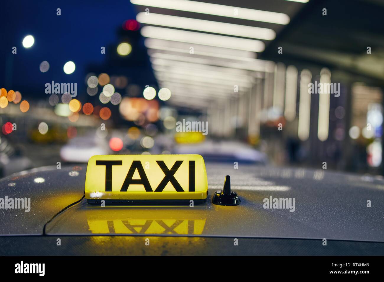 Lighting taxi sign on the roof of car against airport terminal at night